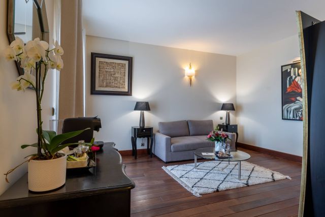 Gemütliches Wohnzimmer mit einem grauen Sofa, eleganter Dekoration, Blumen und warmem Licht, das eine einladende Atmosphäre schafft.