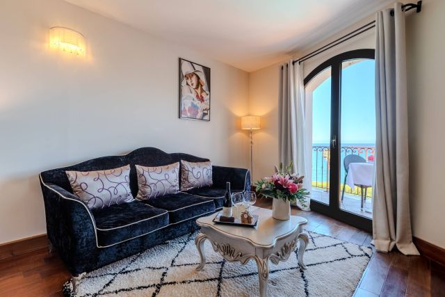 Salon chic avec un canapé noir, une décoration florale et une vue imprenable sur l'océan à travers une porte-balcón.