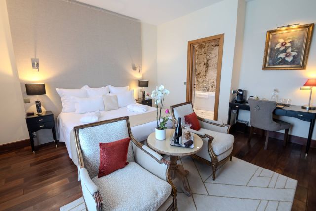 A stylish hôtel room featuring a bed, seating area, desk, and a bathroom door in a cosy, elegant design.