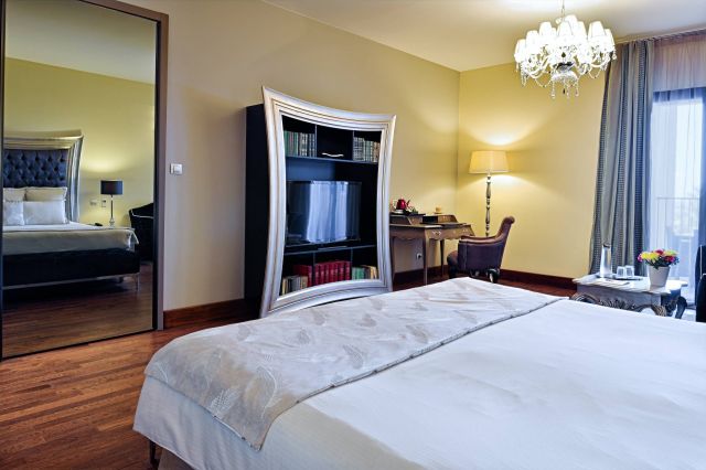 Chambre d'hôtel sophistiquée avec un lit au style raffiné, un décor élégant et une bibliothèque incurvée unique avec un miroir.