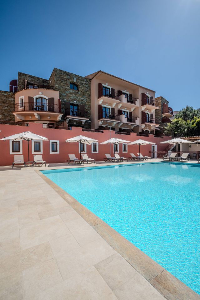 Une zone de piscine sereine avec des chaises longues, ombragée par des parasols, et un bâtiment élégant en arrière-plan sous un ciel bleu.