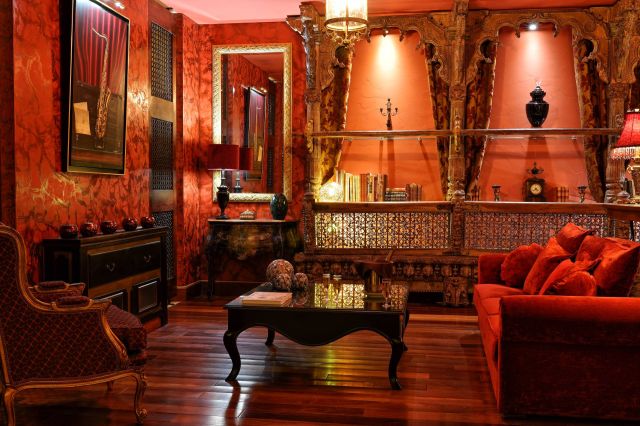 Chambre luxueuse aux riches teintes rouges, décor orné, mobilier élégant et accents artistiques. Atmosphère chaleureuse et accueillante.