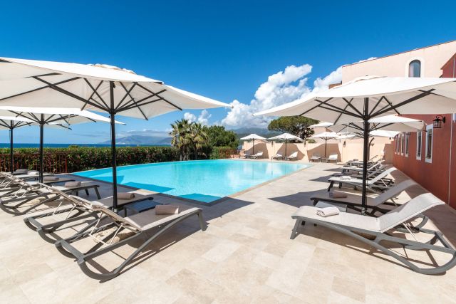 Eine ruhige Poolszene mit Liegen und Sonnenschirmen, vor einem strahlend blauen Himmel und üppigem Grün.