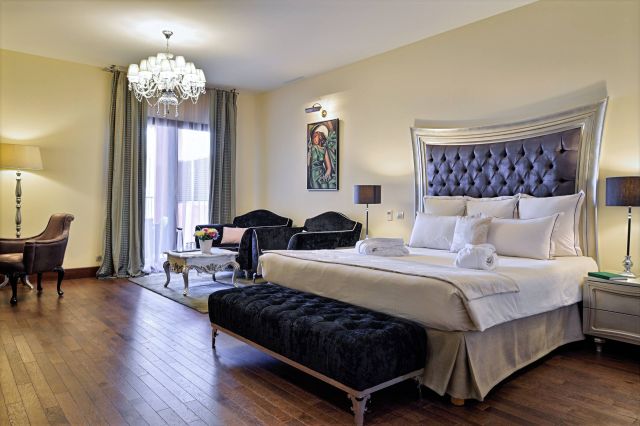 Chambre d'hôtel luxueuse avec un lit moelleux, des meubles élégants, un lustre et de la lumière naturelle provenant de grandes fenêtres.