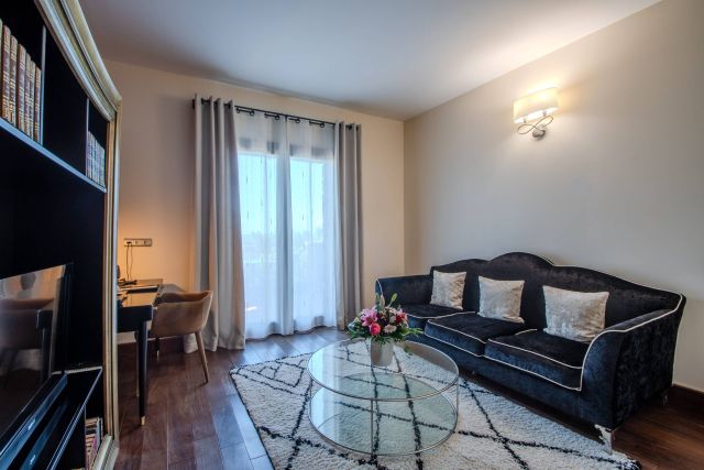 Ein gemütliches Wohnzimmer verfügt über ein dunkles Sofa, einen Glastisch und ein helles Fenster mit Vorhängen.