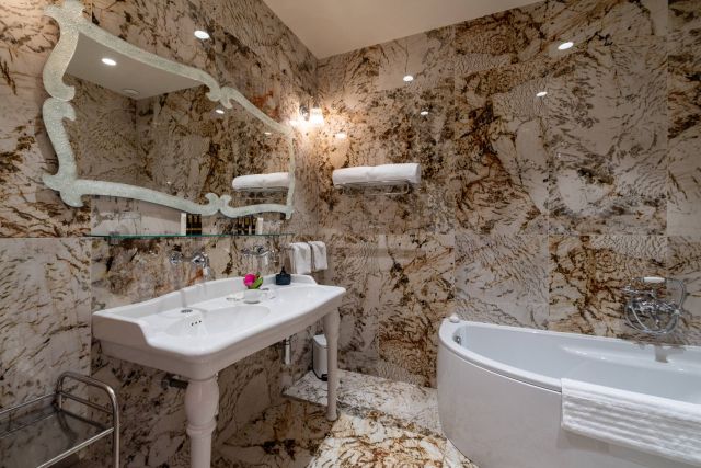 Salle de bains luxueuse avec des murs en marbre, un miroir élégant, un lavabo moderne et une baignoire au design soigné agrémentée de touches florales.