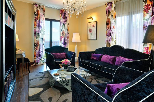 A stylish living room with floral curtains, dark sofas, a chandelier, and a coffee table set for tea.
