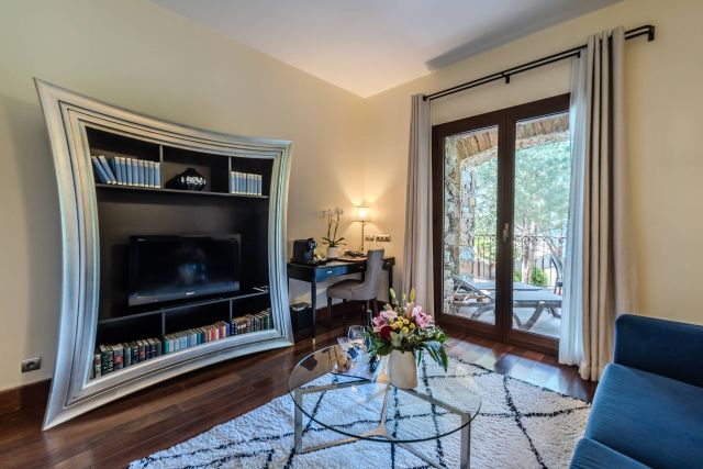 Salon cosy avec une unité TV élégante, une table en verre, des fleurs et une vue sur le balcon. Éclairage chaleureux et décoration moderne.