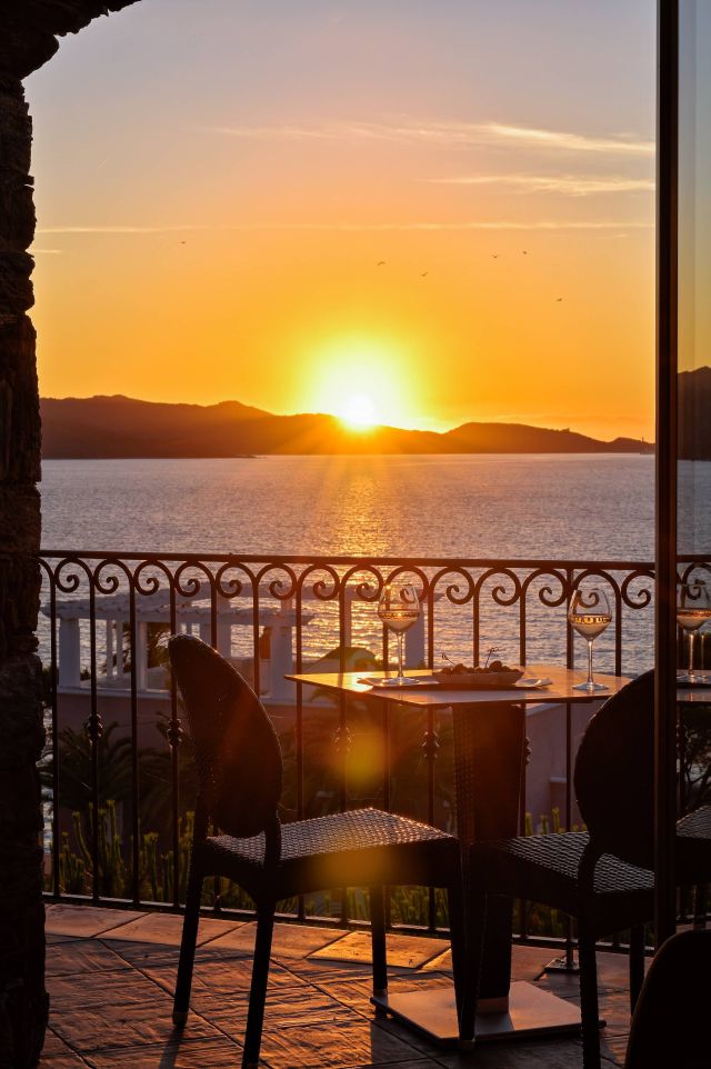 Une vue tranquille sur le coucher de soleil au-dessus de l'eau, avec une table garnie de boissons et un paysage magnifique en arrière-plan.