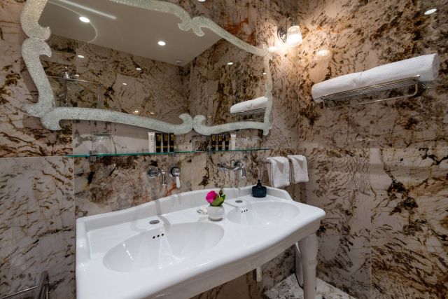 Elegantes Badezimmer mit Doppelwaschbecken, Marmormauern, dekorativem Spiegel und stilvollen Akzenten.