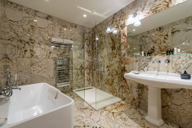 Salle de bains luxueuse avec des murs en marbre, une douche moderne, une baignoire autoportante et un éclairage élégant.