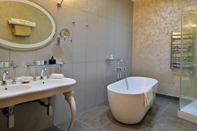 Ein modernes Badezimmer verfügt über eine freistehende Badewanne, ein elegantes Waschbecken, Glasregale und stilvolle Fliesen.