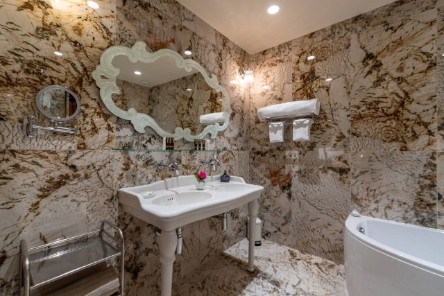 Elegantes Badezimmer mit Marmiwänden, stilvollem Waschbecken, dekorativem Spiegel und einem Hauch von Blumenakzent.