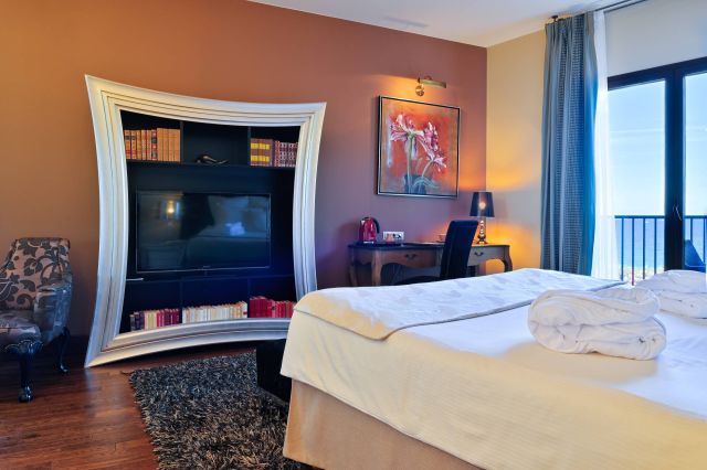 Chambre d'hôtel élégante avec une unité de télévision unique, un coin salon, un bureau et vue sur la mer à travers de grandes fenêtres. Décor confortable et moderne.