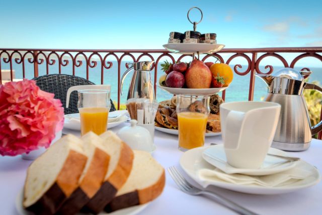 Un magnifique petit-déjeuner composé de fruits, de pâtisseries, de pain et de boissons, avec une vue imprenable sur l'océan.