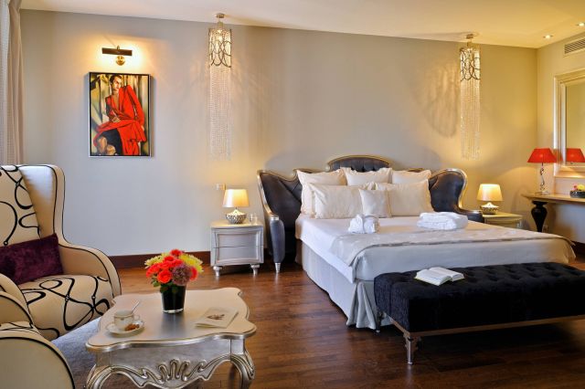 Une chambre luxueuse avec un lit moderne, une décoration élégante, des œuvres d'art et un coin salon confortable agrémenté de fleurs et de rafraîchissements.