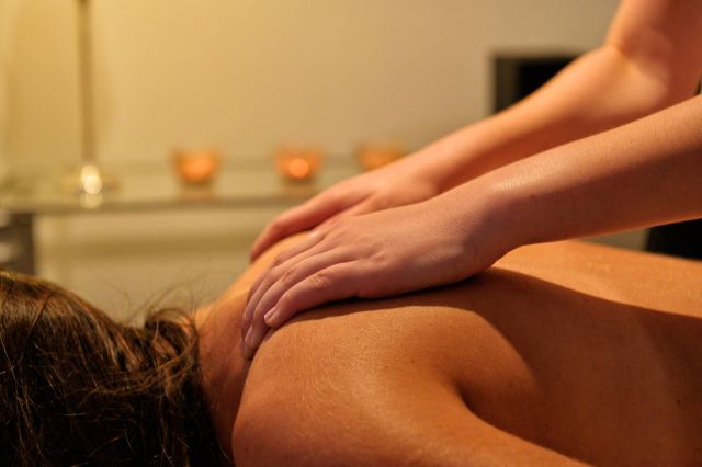 A pair of hands gently massaging a person's back in a serene, softly lit environment.