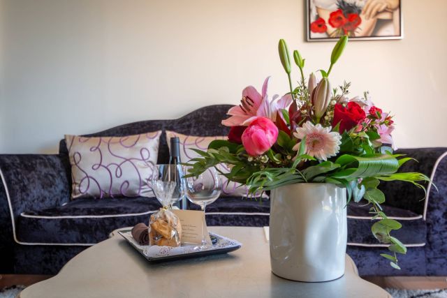 Ein stilvolles Wohnzimmer mit einem floralen Mittelpunkt, Wein und Desserts auf einem Tisch, ergänzt durch elegante Dekoration.