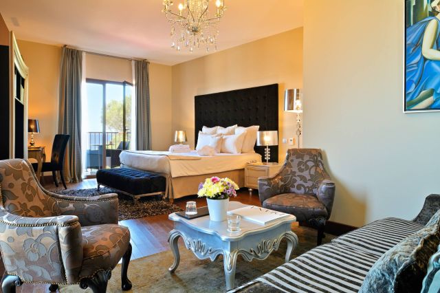 Une chambre élégante avec un grand lit, des meubles raffinés et une vue depuis le balcon, présentant des couleurs douces et une décoration chic.