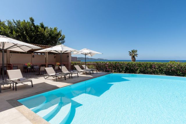 Oasis ensoleillée au bord de la piscine avec des transats, des parasols et des vues sur l'océan sous un ciel bleu clair. La détente vous attend !