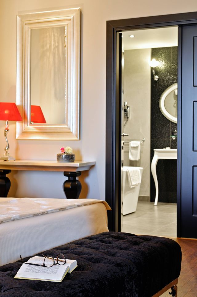 Une chambre élégante avec un ottoman noir, un livre et des lunettes, dotée d'une lampe cosy et d'un aperçu d'une salle de bain moderne.