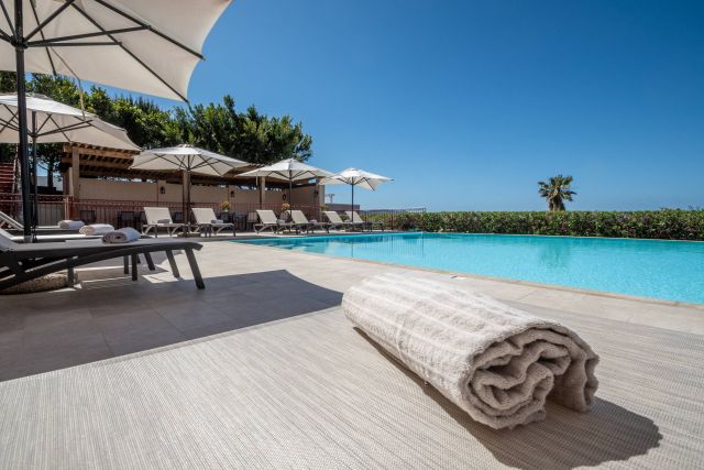 A serene poolside scene with sun loungers, umbrellas, and a rolled towel, under a clear blue sky. Perfect for relaxation.