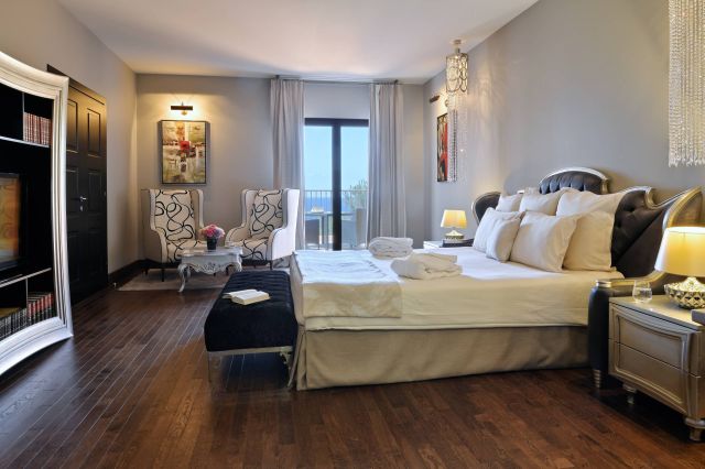 Elegantes Schlafzimmer mit einem Kingsize-Bett, stilvollen Armchairs und einem Blick, ausgestattet mit modernem Dekor und warmem Licht.