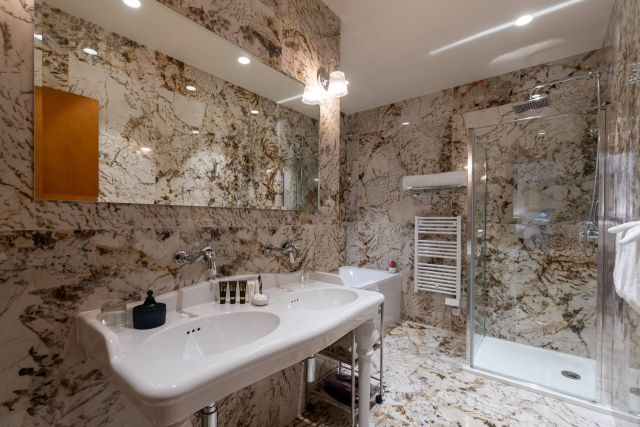 Salle de bains luxueuse avec de élégants murs en marbre, double vasque, douche moderne et éclairage stylé.