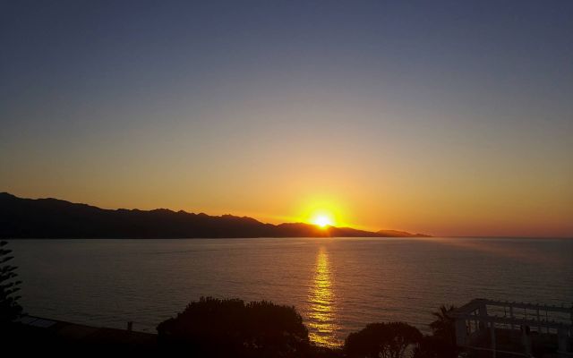 Un coucher de soleil serein sur des eaux calmes, avec des rayons dorés se reflétant sur la mer et des montagnes en silhouette en arrière-plan.